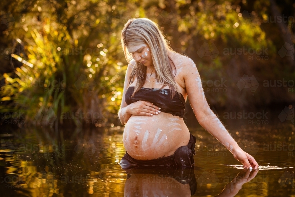 Peaceful scene with pregnant aboriginal woman in still water with reflection - Australian Stock Image