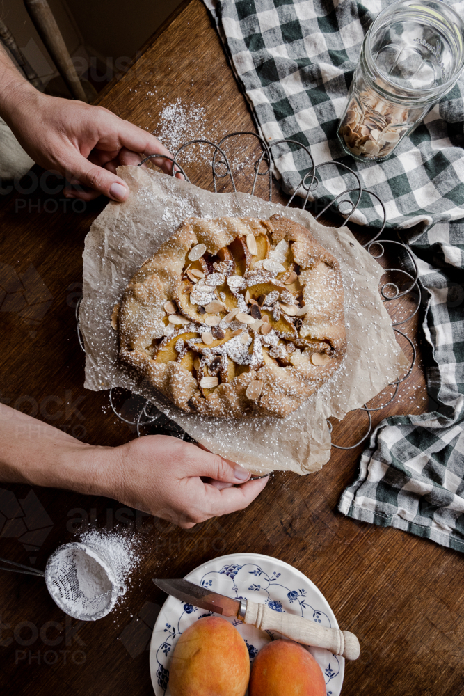 peach tart with hands on a timber tabletop - Australian Stock Image