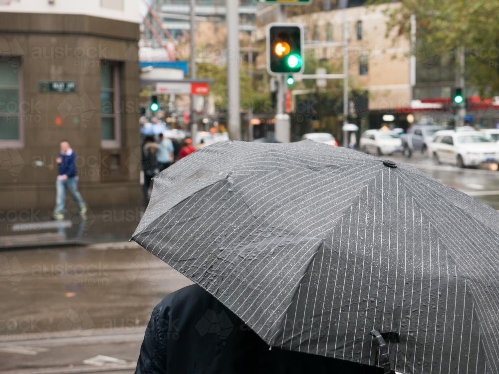 Pedestrians with umbrella wait at traffic lights on a rainy day - Australian Stock Image