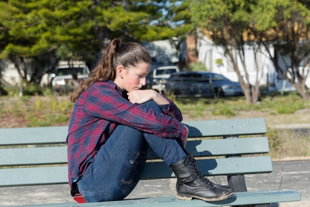 Pensive teenager sitting on park bench - Australian Stock Image