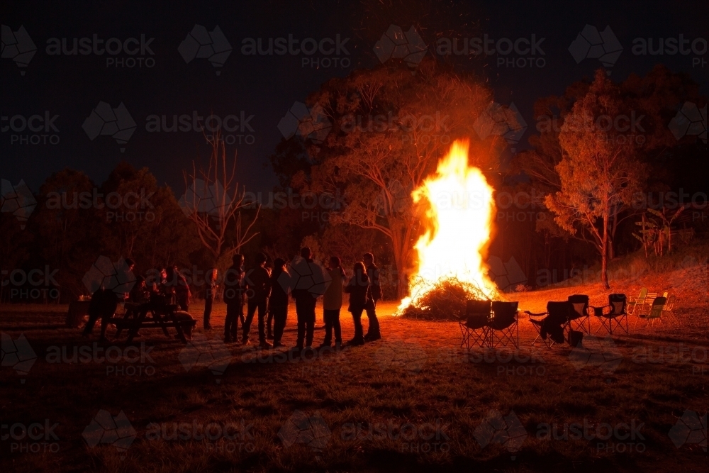 People and chairs around a blazing bonfire at night - Australian Stock Image