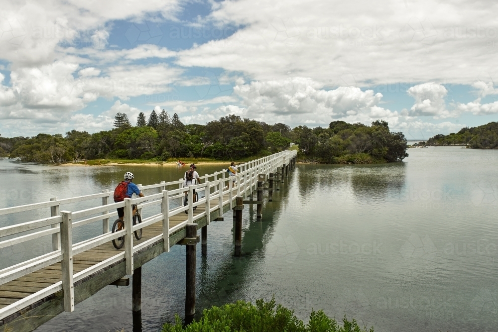 People cycling and fishing on a bridge at a coastal creek - Australian Stock Image