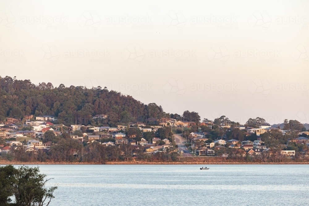 People fishing in boat on Lake Macquarie with houses on hill in background - Australian Stock Image