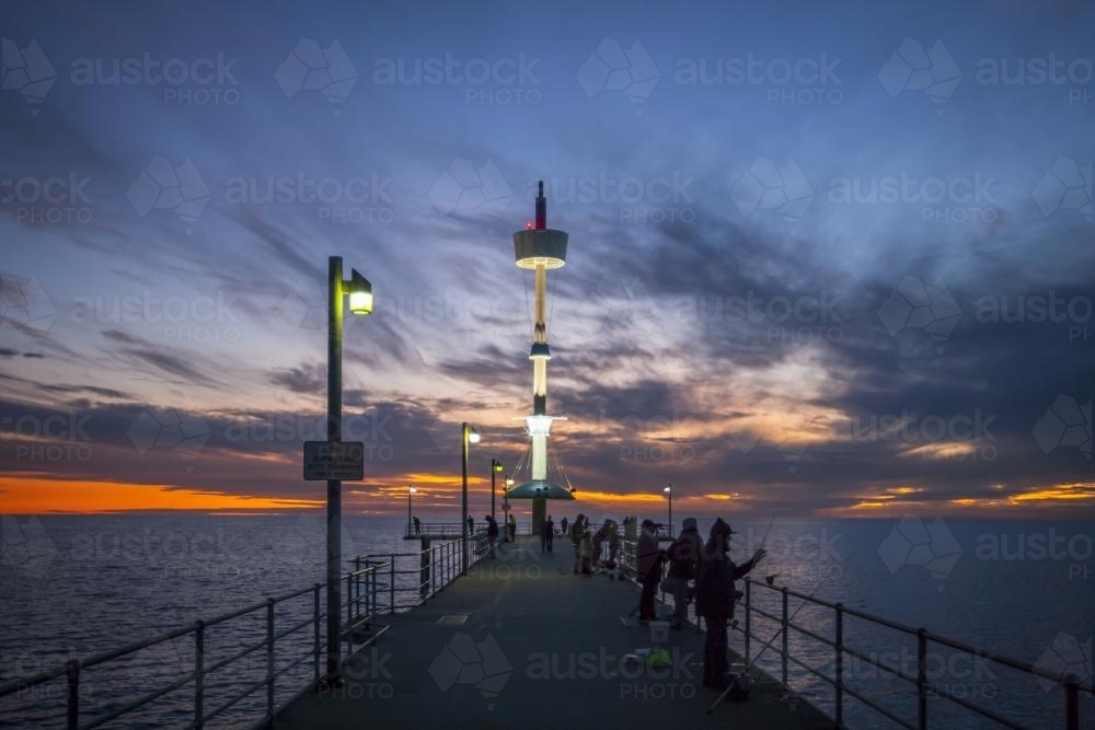 People fisshing off Brighton Jetty on a dark sunset - Australian Stock Image