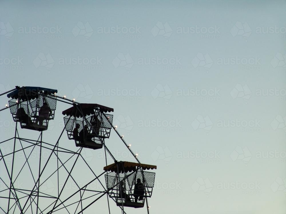 People in a ferris wheel silhouetted against a blue sky - Australian Stock Image