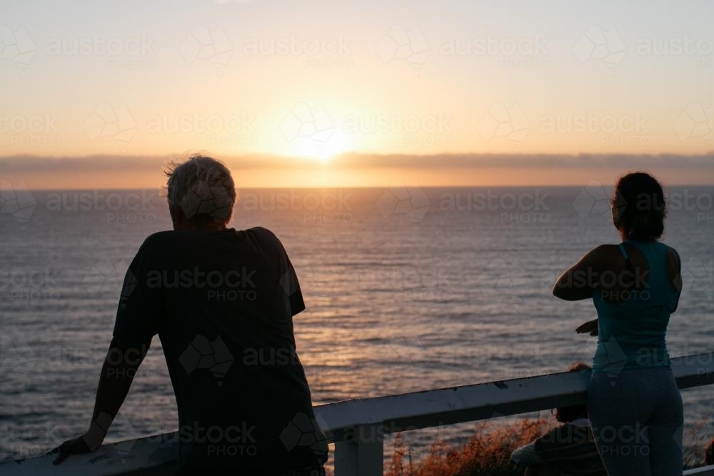 People in silhouette watching the sunrise over water - Australian Stock Image