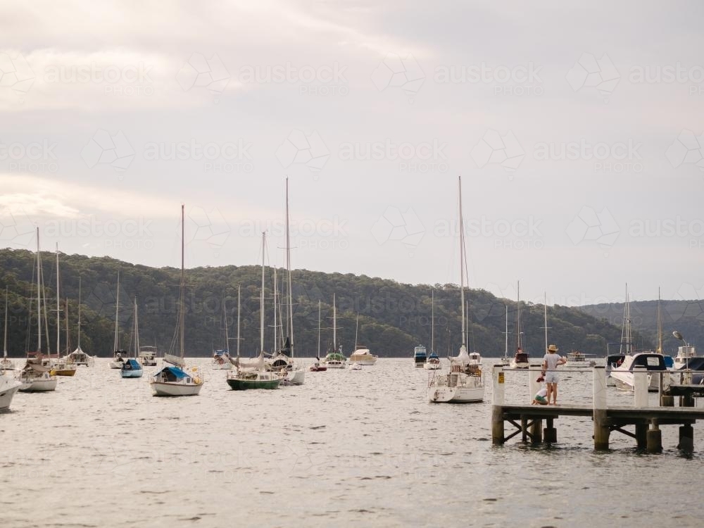 People on jetty and sailing boats with hills in the background - Australian Stock Image
