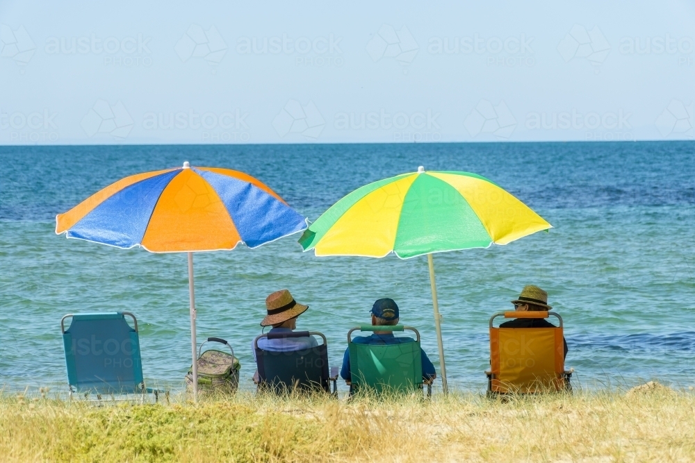 Image of People sitting in beach chairs under colourful umbrellas