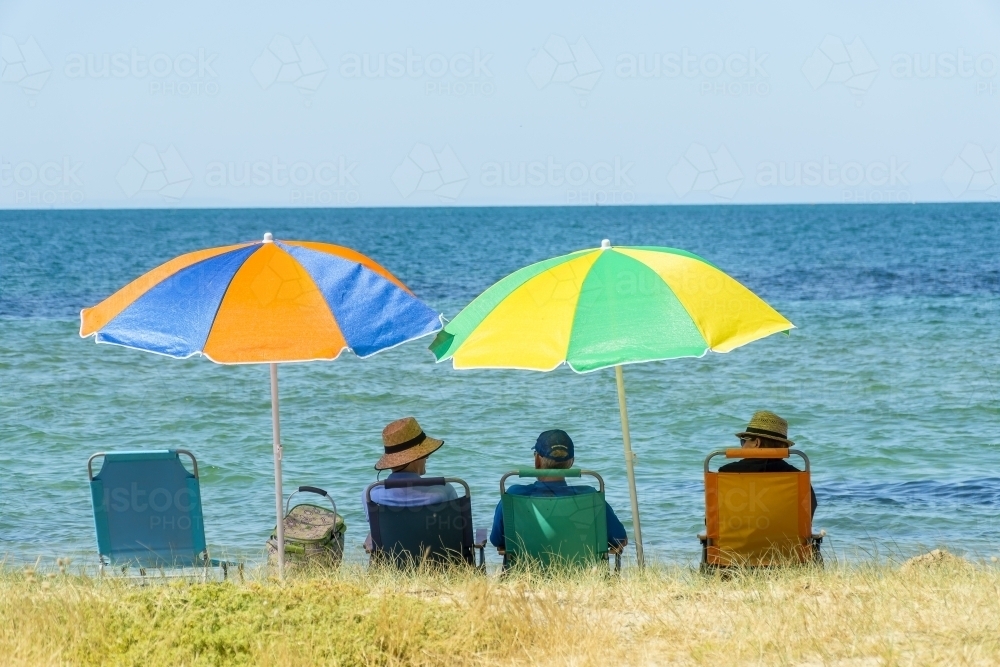 People sitting in beach chairs under colourful umbrellas - Australian Stock Image