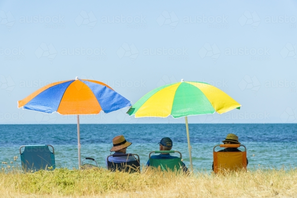 Image of People sitting in beach chairs under colourful umbrellas