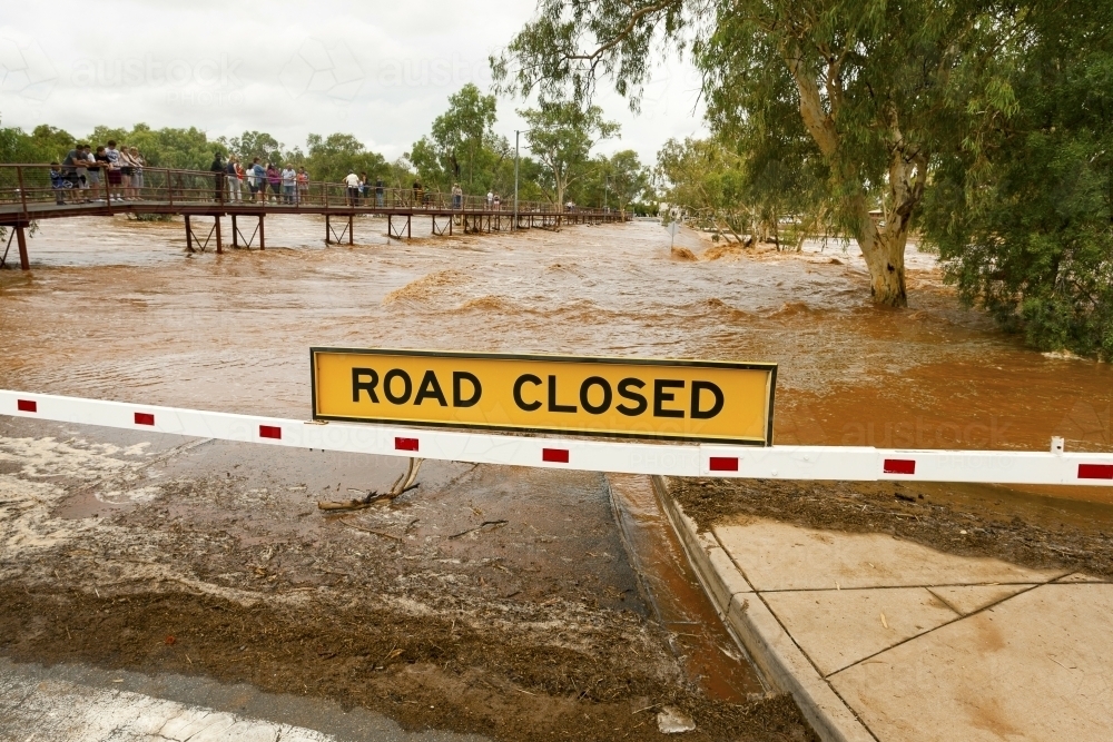People standing along bridge beside road closed due to flooding - Australian Stock Image