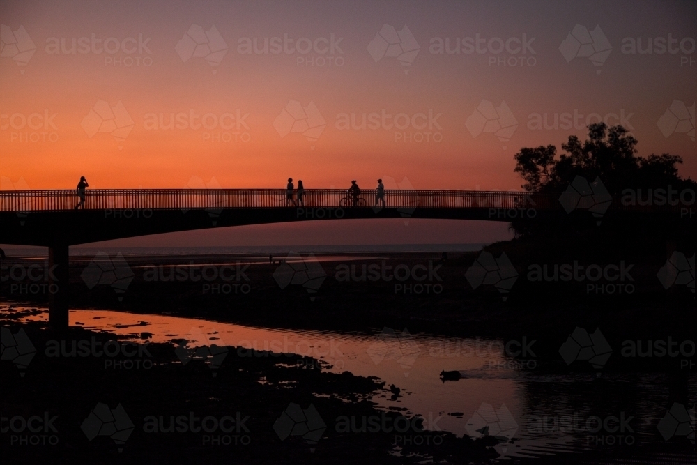 People walking across bridge at sunset - Australian Stock Image