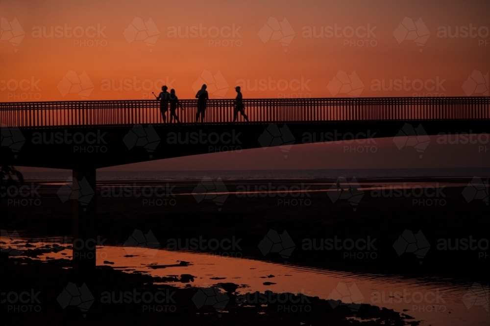 People walking across bridge at sunset - Australian Stock Image