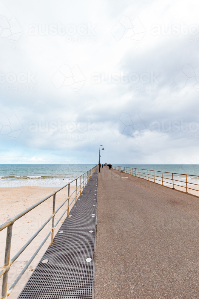 People walking along Glenelg Jetty on a cloudy winter day - Australian Stock Image