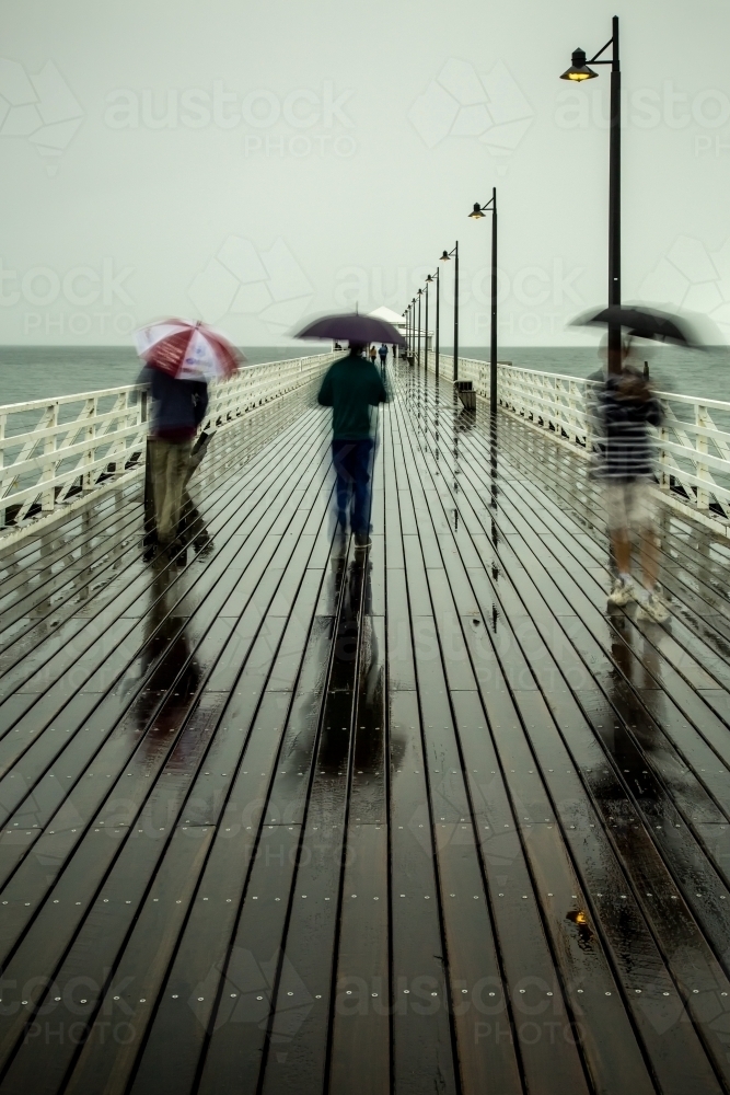 People walking on a pier with umbrellas on a rainy day. - Australian Stock Image
