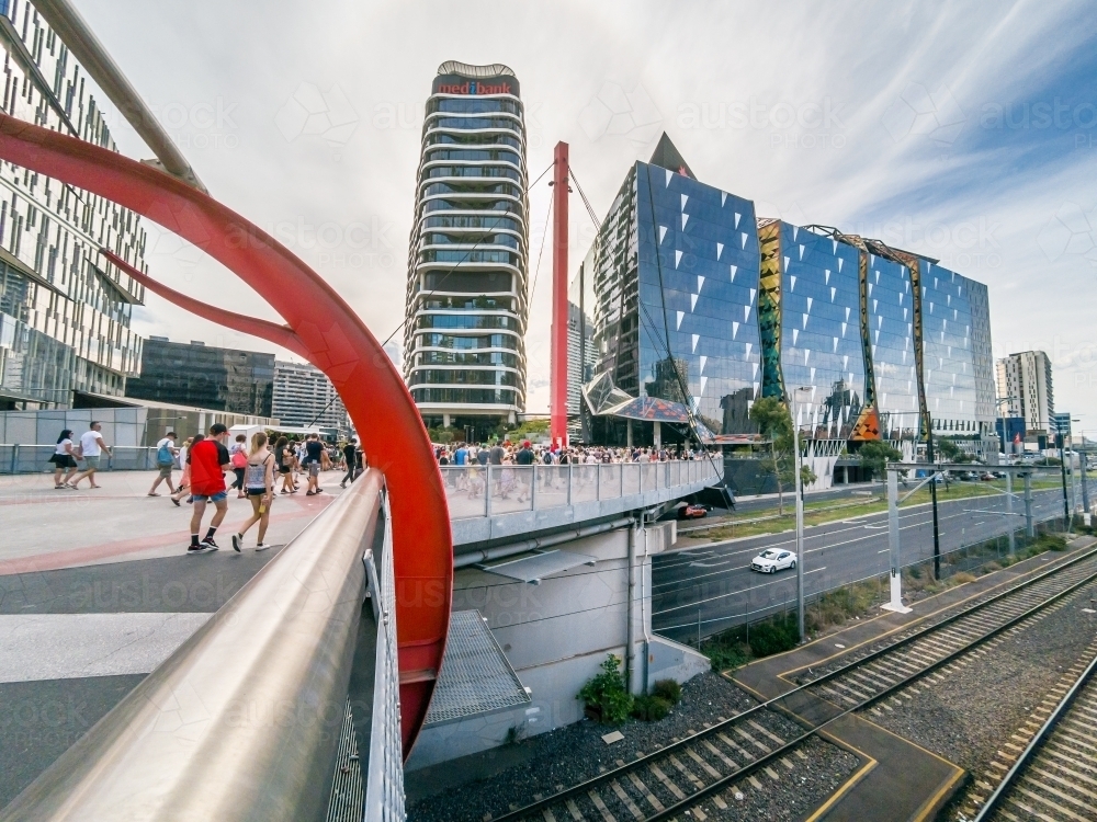 People walking on a transit bridge over roads and railway lines towards city buildings - Australian Stock Image