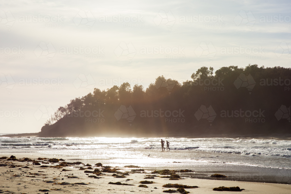 People walking on beach at sunset with trees in background - Australian Stock Image