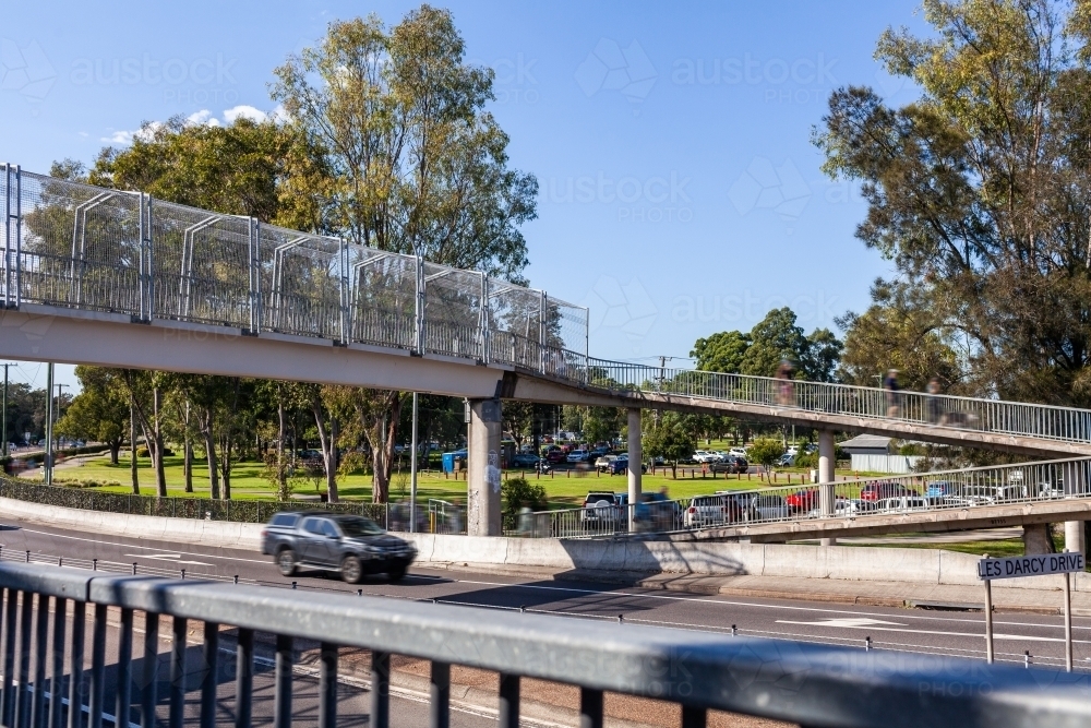 People walking on overpass bridge for pedestrians crossing busy city road - Australian Stock Image