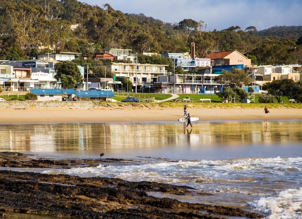 People walking on the beach at a coastal town with shops in background - Australian Stock Image