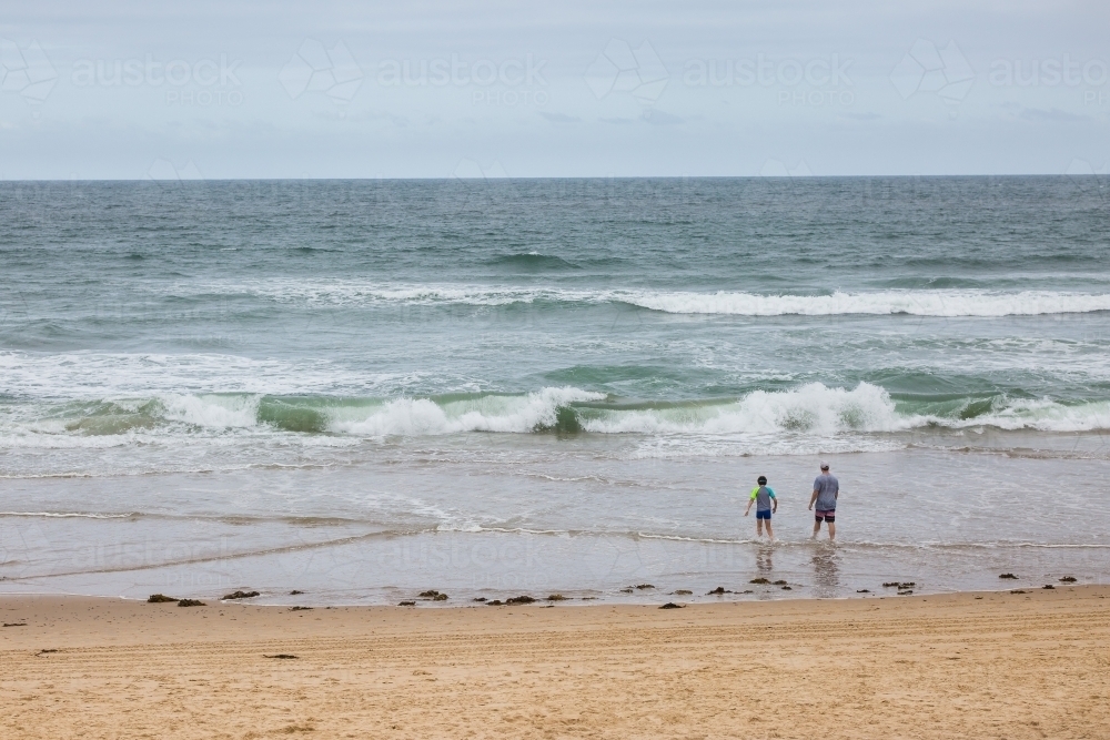 People walking towards waves on beach from behind - Australian Stock Image