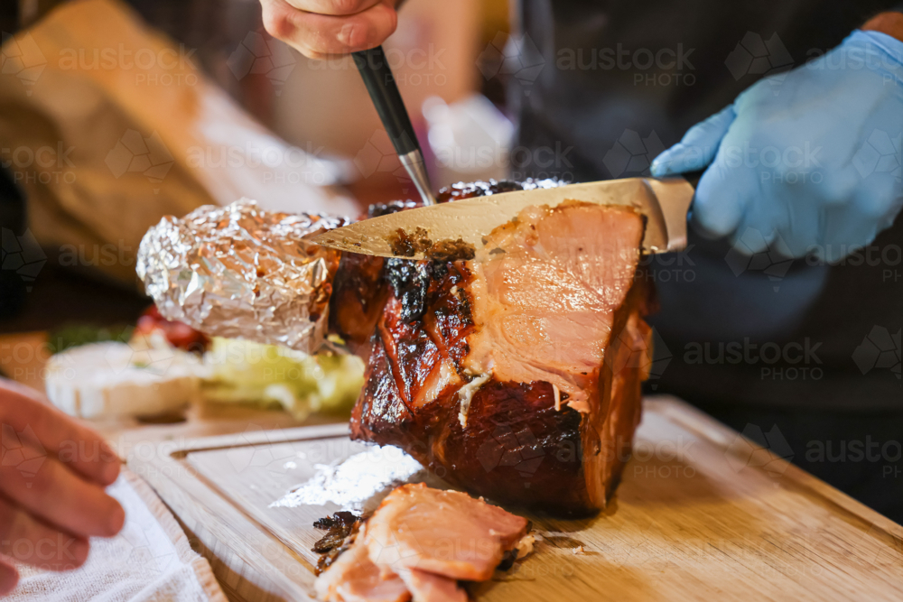 Person carving glazed Christmas ham on wooden cutting board - Australian Stock Image