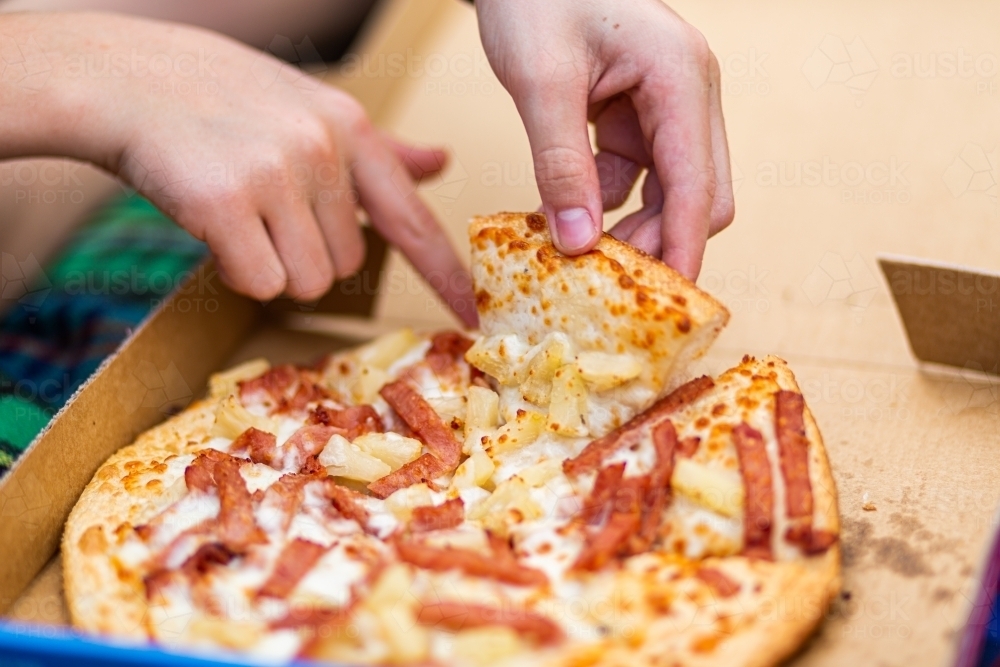 Person grabbing the first slice of pizza from delivery box - Australian Stock Image
