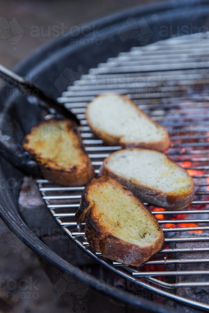 Person grilling thick slices of bread on hot coals on a bbq outside - Australian Stock Image
