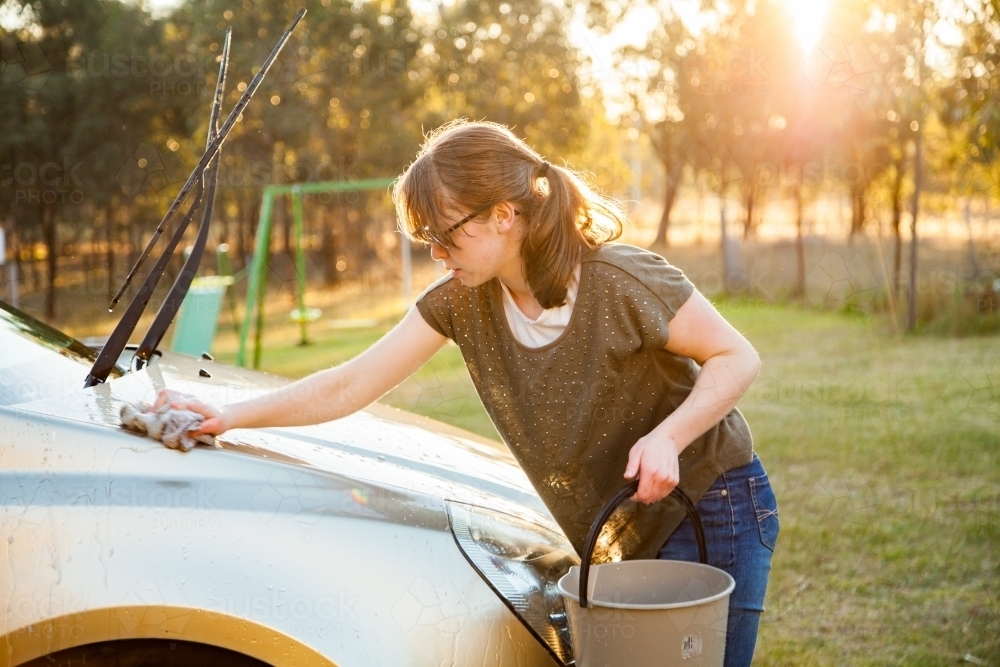 Person hand washing front of family car in backyard in natural light flare - Australian Stock Image