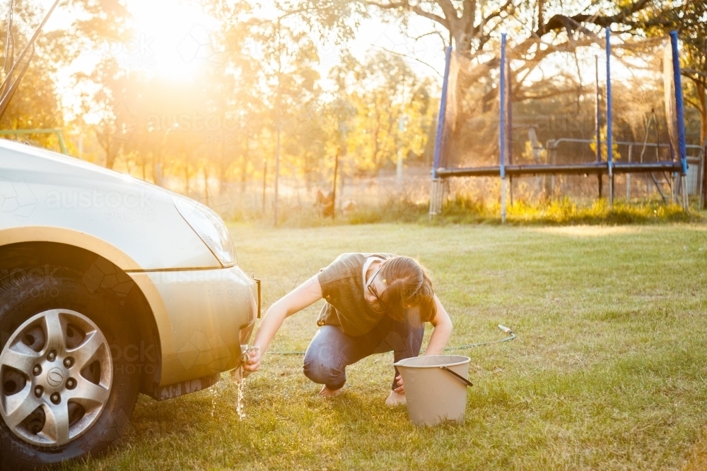 Person hand washing front of family car in backyard in natural light flare - Australian Stock Image