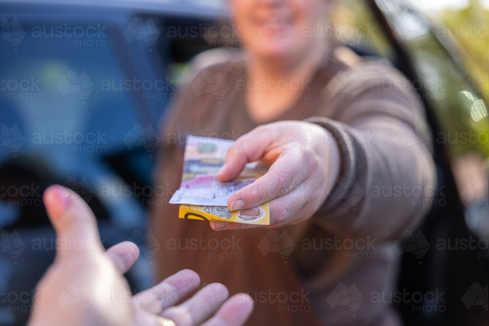 Person handing over cash bank notes to another hand during financial transaction outdoors - Australian Stock Image