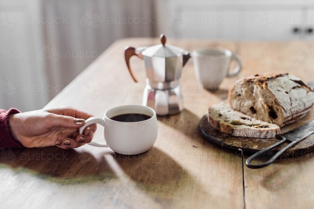 Person having coffee and artisan bread with stovetop espresso maker on table. - Australian Stock Image