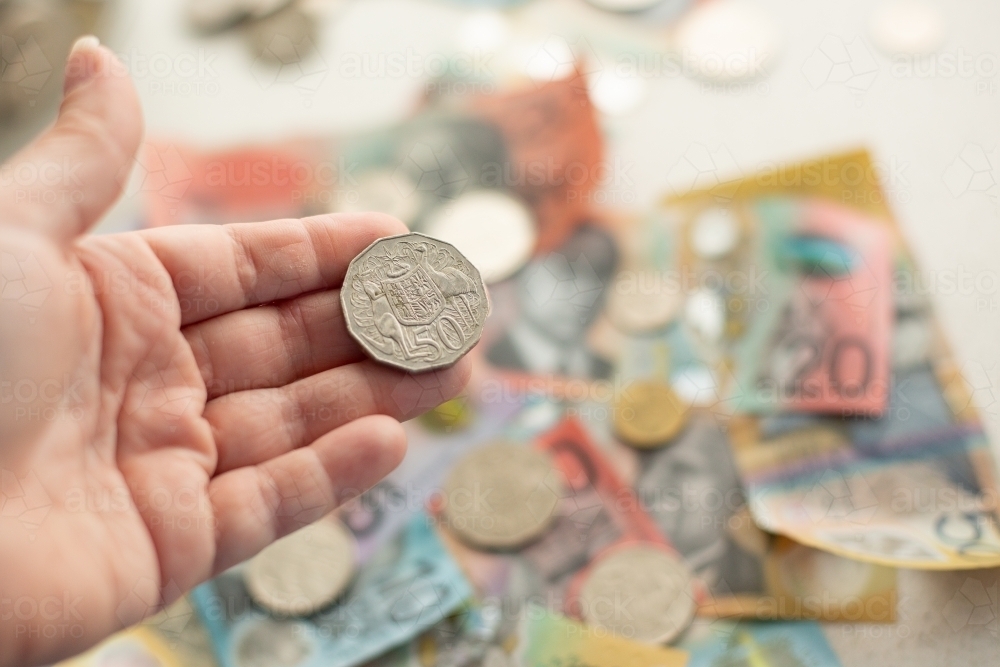 person holding an Australian 50 cent piece with other money in the background - Australian Stock Image