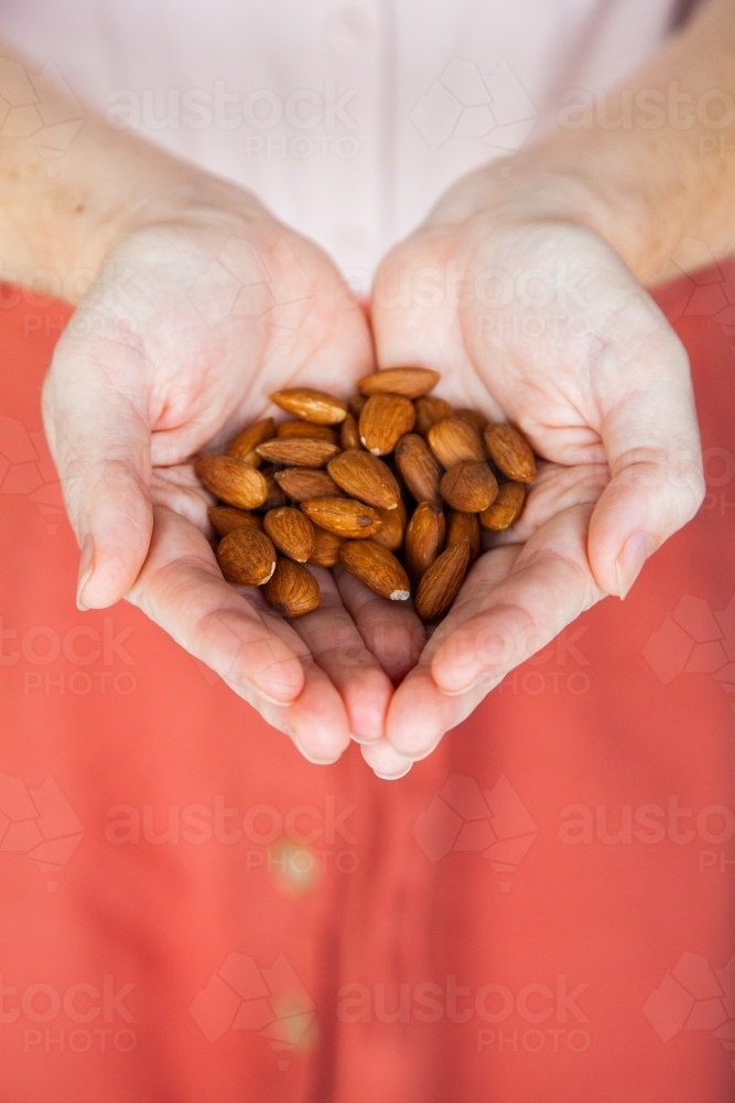 Person holding healthy snack of almond nuts in her hands - Australian Stock Image