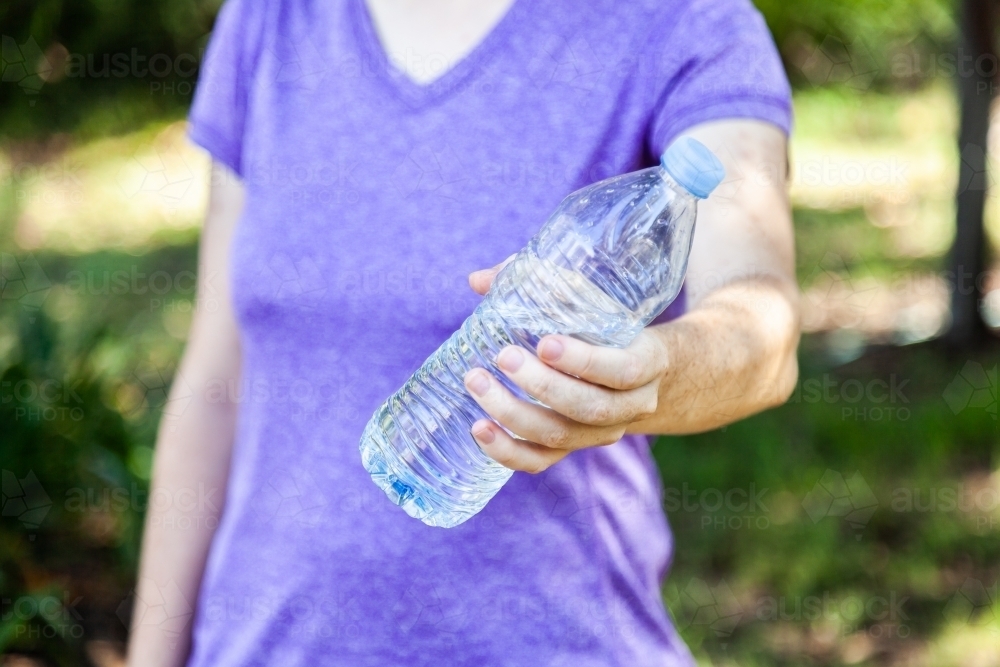Person holding out plastic water bottle with water in it - Australian Stock Image