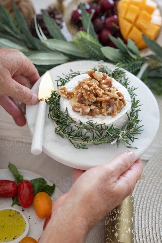 Person holding platter of camembert cheese at Christmas-decorated table - Australian Stock Image