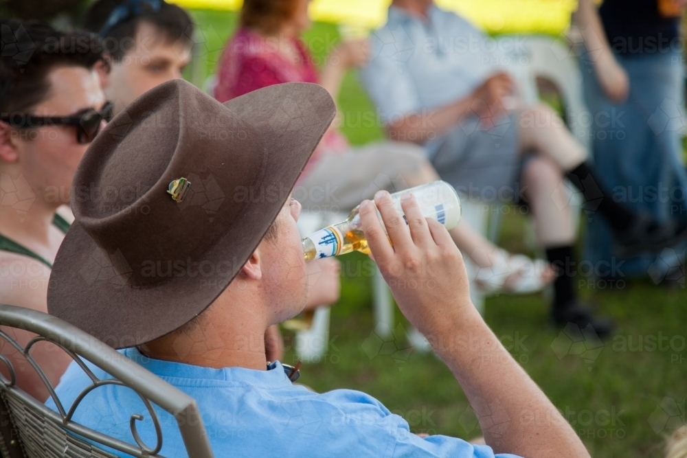 Image of Person in akubra hat drinking beer outside