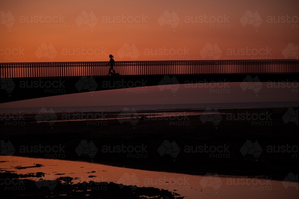 Person jogging across bridge at sunset - Australian Stock Image