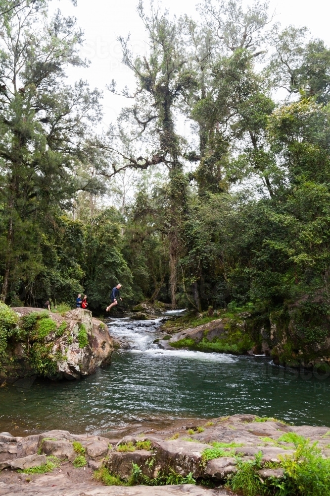 Person jumping off a riverside rock into creek - Australian Stock Image