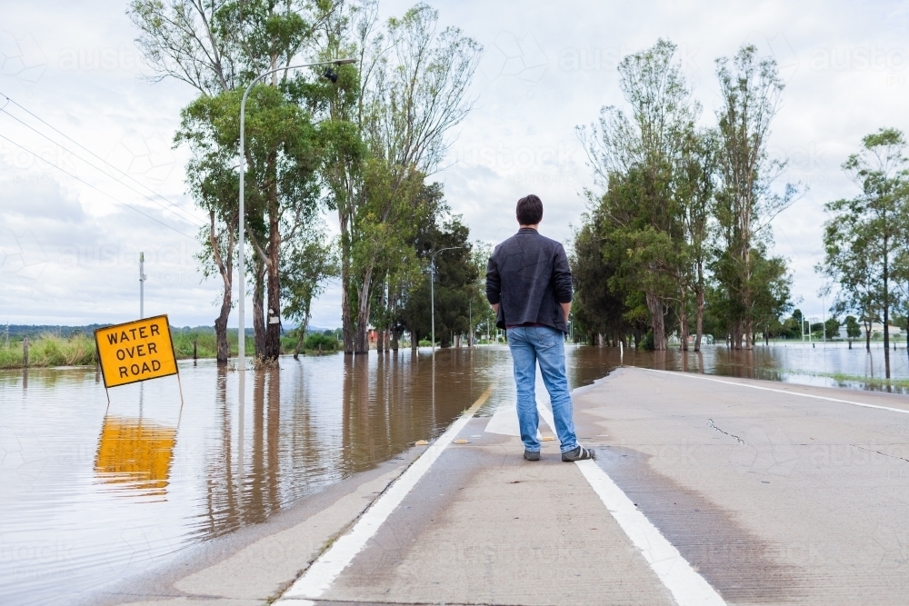 Person looking at floodwaters over road cutting off access via New England Highway through singleton - Australian Stock Image