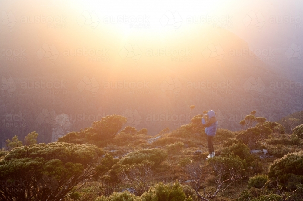 Person looking through binoculars at mountain range at sunset - Australian Stock Image