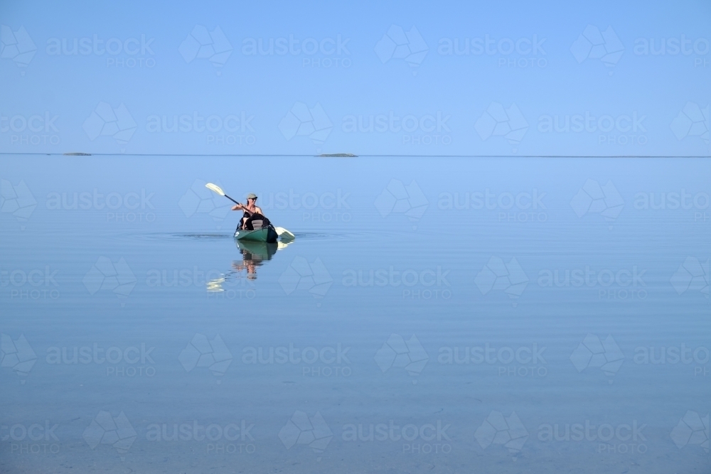 Person paddling kayak on flat glassy ocean - Australian Stock Image