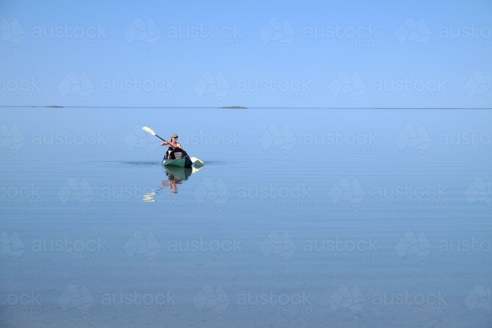 Person paddling kayak on flat glassy ocean - Australian Stock Image