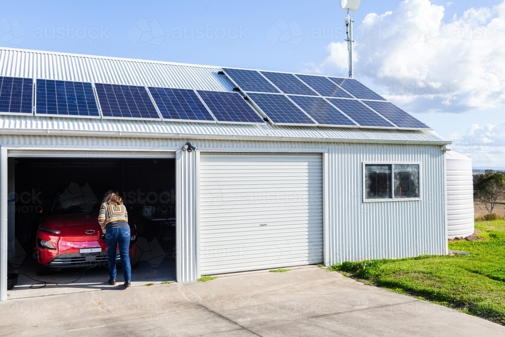 Person plugging in electric vehicle car to charge with renewable energy from wind and solar power - Australian Stock Image
