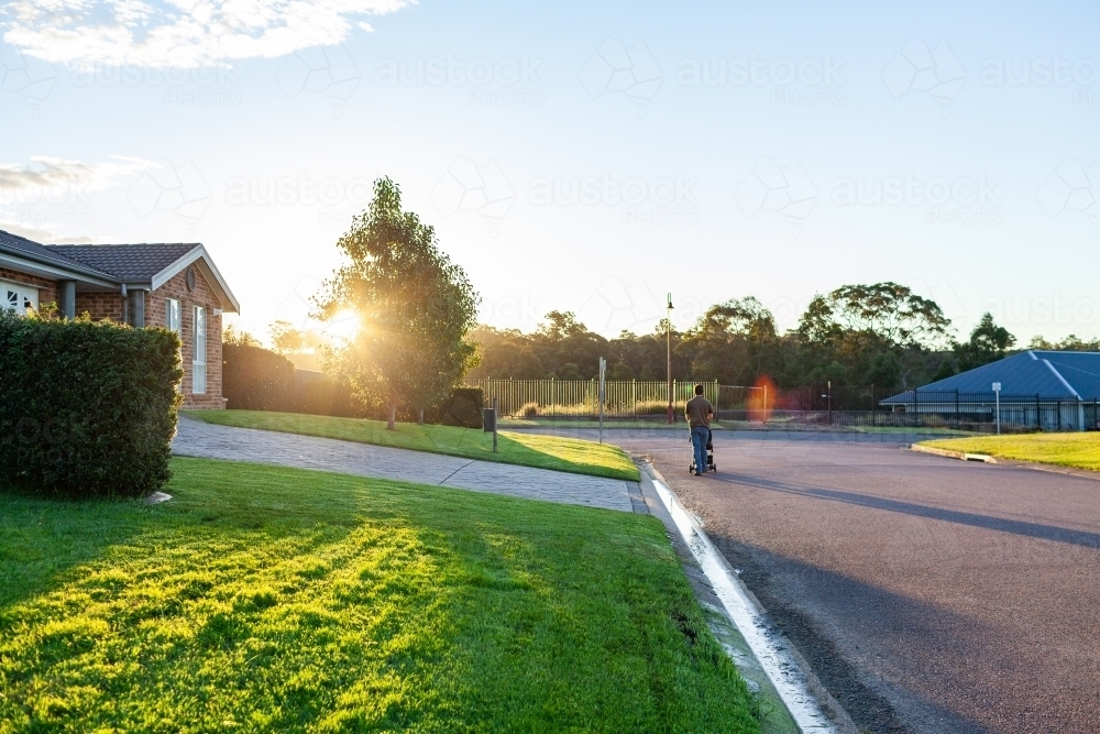 Person pushing pram down suburban street at sunset - Australian Stock Image