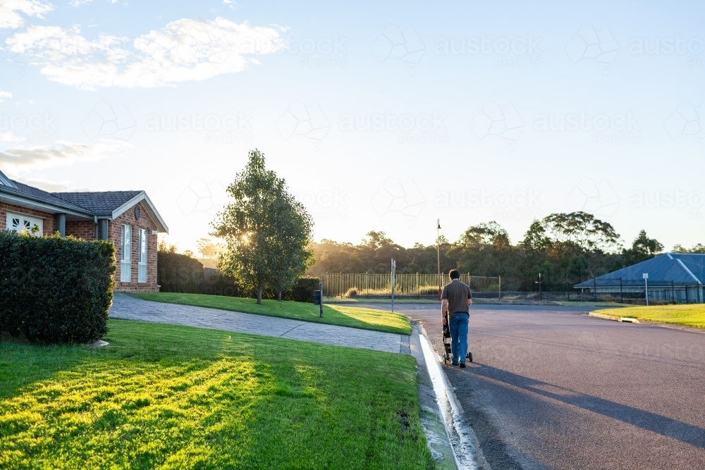 Person pushing pram down suburban street at sunset - Australian Stock Image