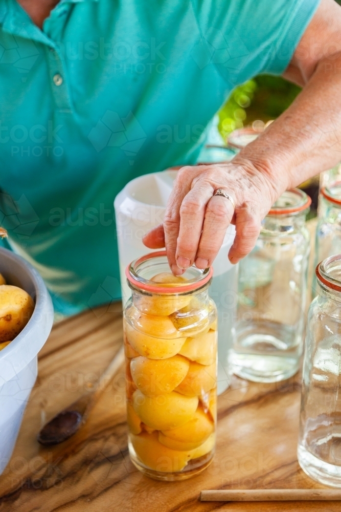 Image of Person putting fruit in jar preserving fresh apricots