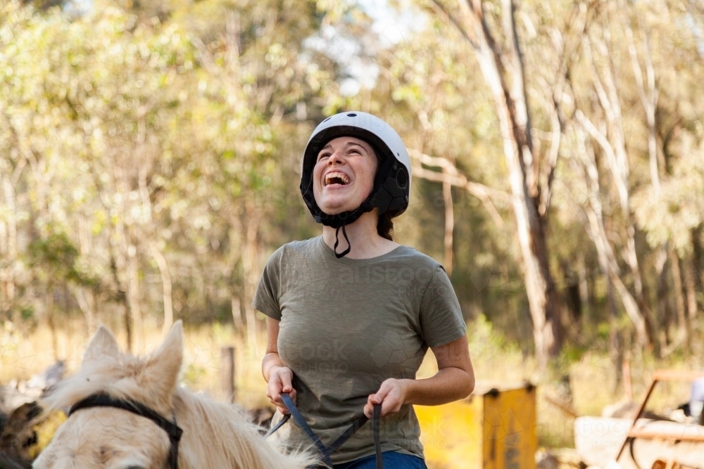 Person riding horse laughing as she canters outside - Australian Stock Image