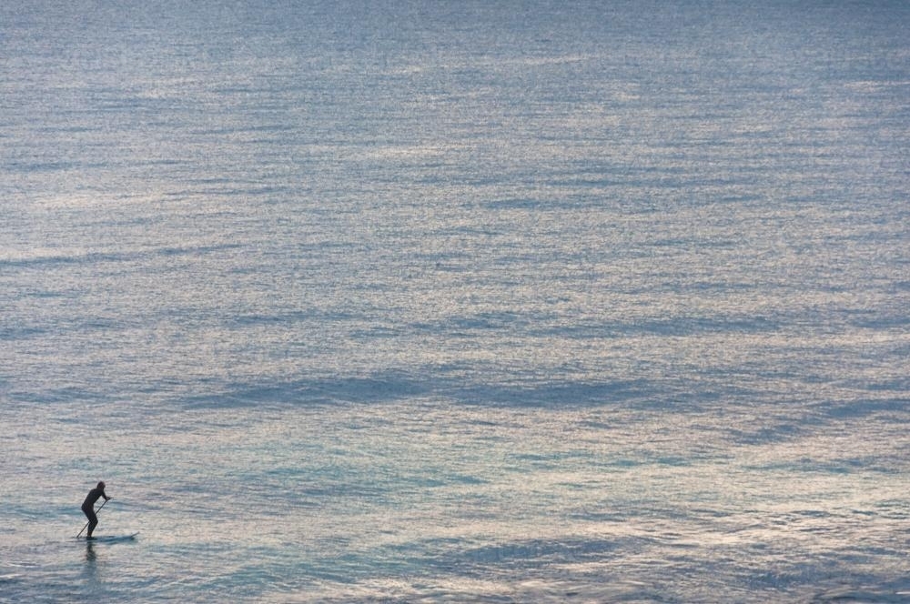 Person Riding on Stand up Paddleboard in Distance - Australian Stock Image