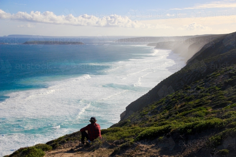 Person sitting on steep coastal cliff - Australian Stock Image