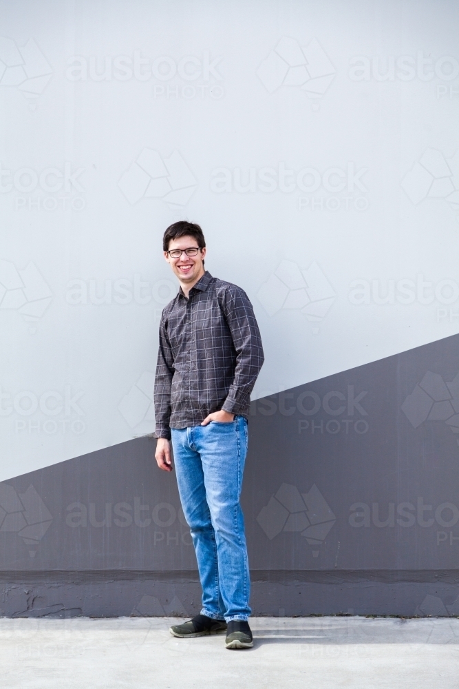 Person standing beside wall in urban area - full length body shot of young man - Australian Stock Image